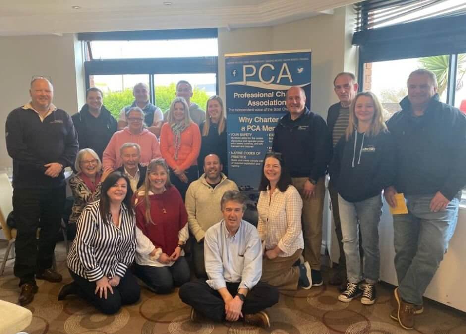 Members of the Professional Charter Association standing next to a banner March 2023.